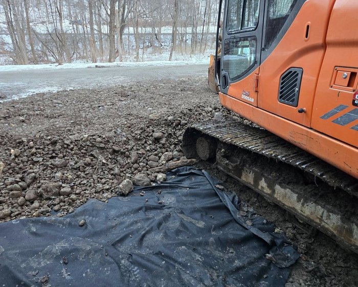 Stone base spread over geotextile fabric next to an excavator