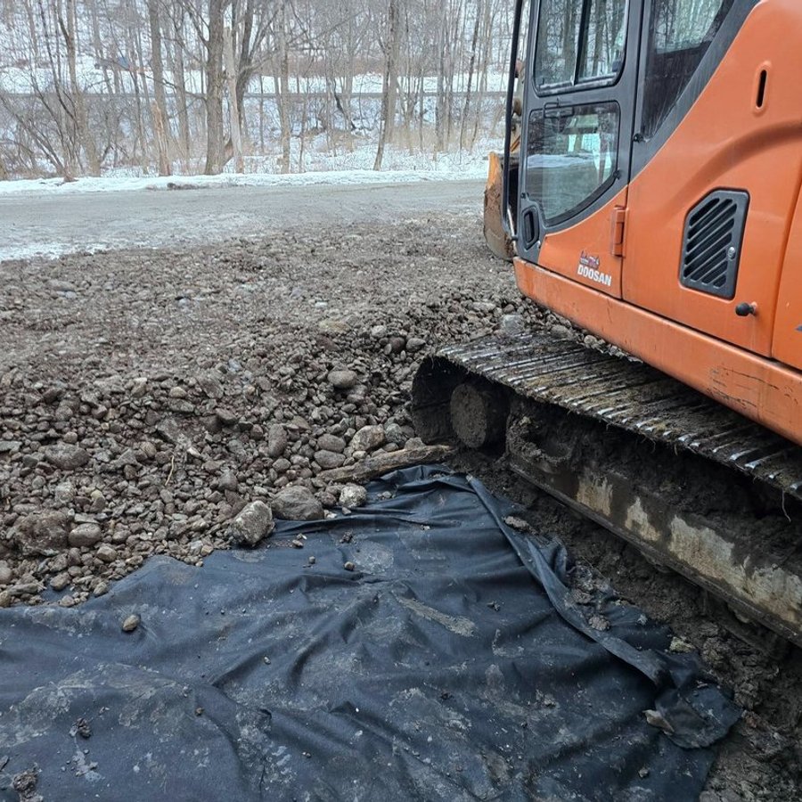 Stone base spread over geotextile fabric next to an excavator