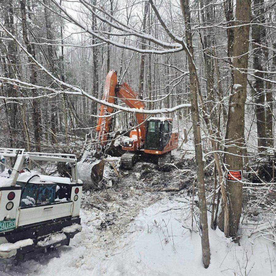 Excavator working a clearing job in winter woods beside a service truck